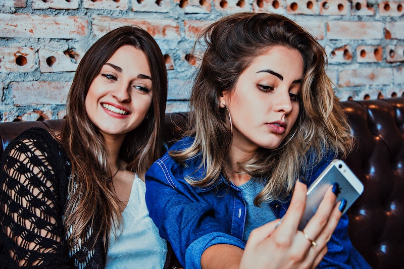 Two women sitting on a couch looking at their phones.