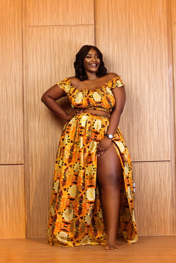 A smiling woman in a yellow two-piece outfit poses against a wooden background.