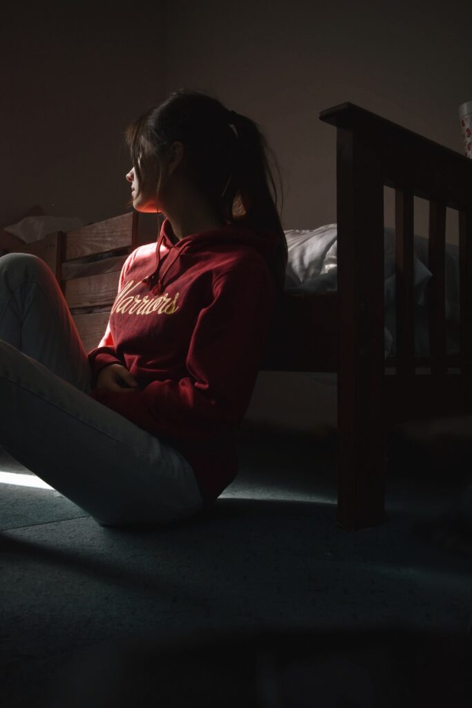 A girl sitting on the floor next to a bed.