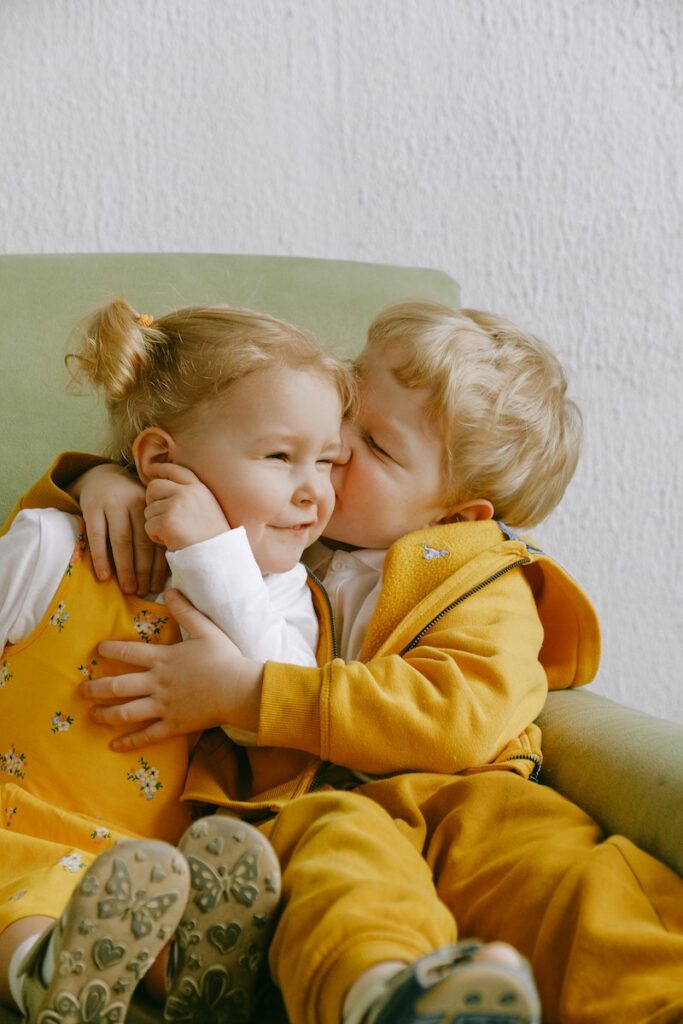 Two children hugging on a green chair.