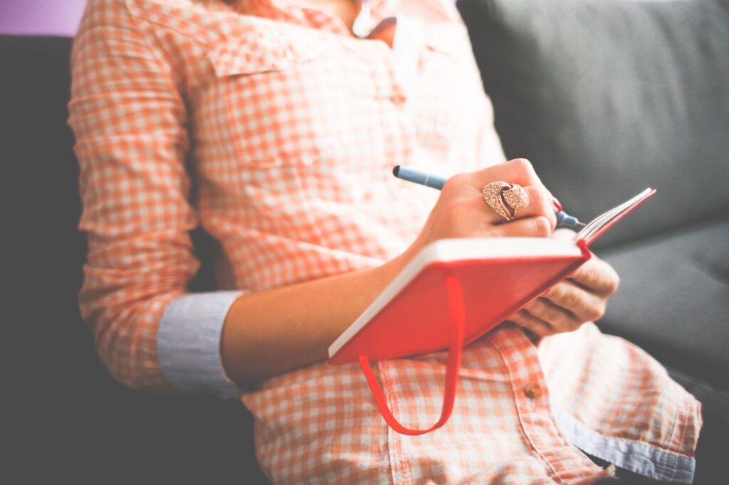 A woman writing in a notebook on a couch.