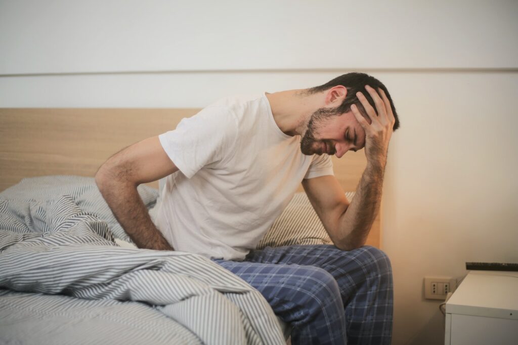 A man in pajamas is sitting in bed with his head on his head.